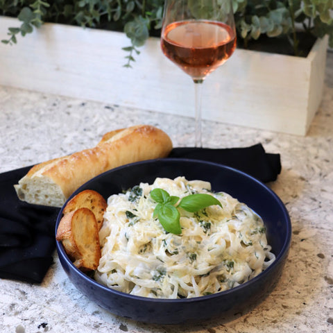 Spinach Fettuccine Alfredo in blue bowl made with organic, low carb GoSkinny Noodles Fettuccine; beside baguette and glass of rose wine